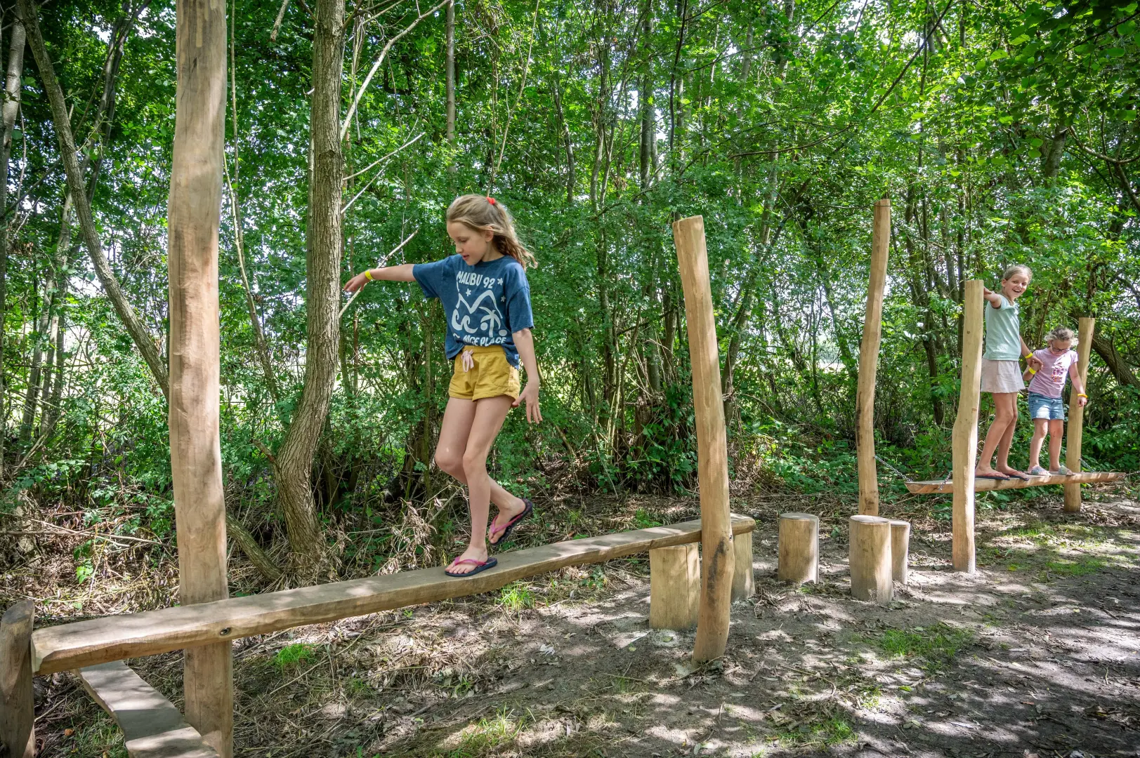 Een meisje loopt in de zomer over een houten parcours