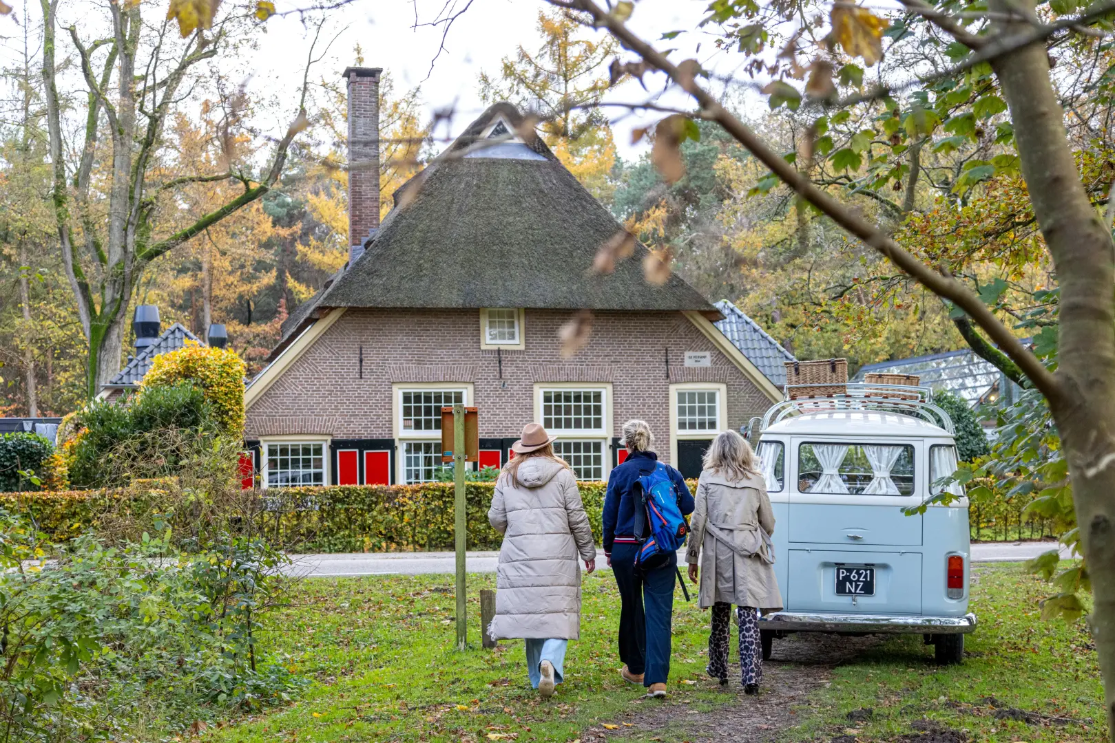 3 vrouwen lopen op een pad met herfstbladeren en een old timer volkswagenbusje