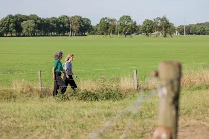 2 vrouwen wandelen door een uitgestrekt weidegebied in de zomer
