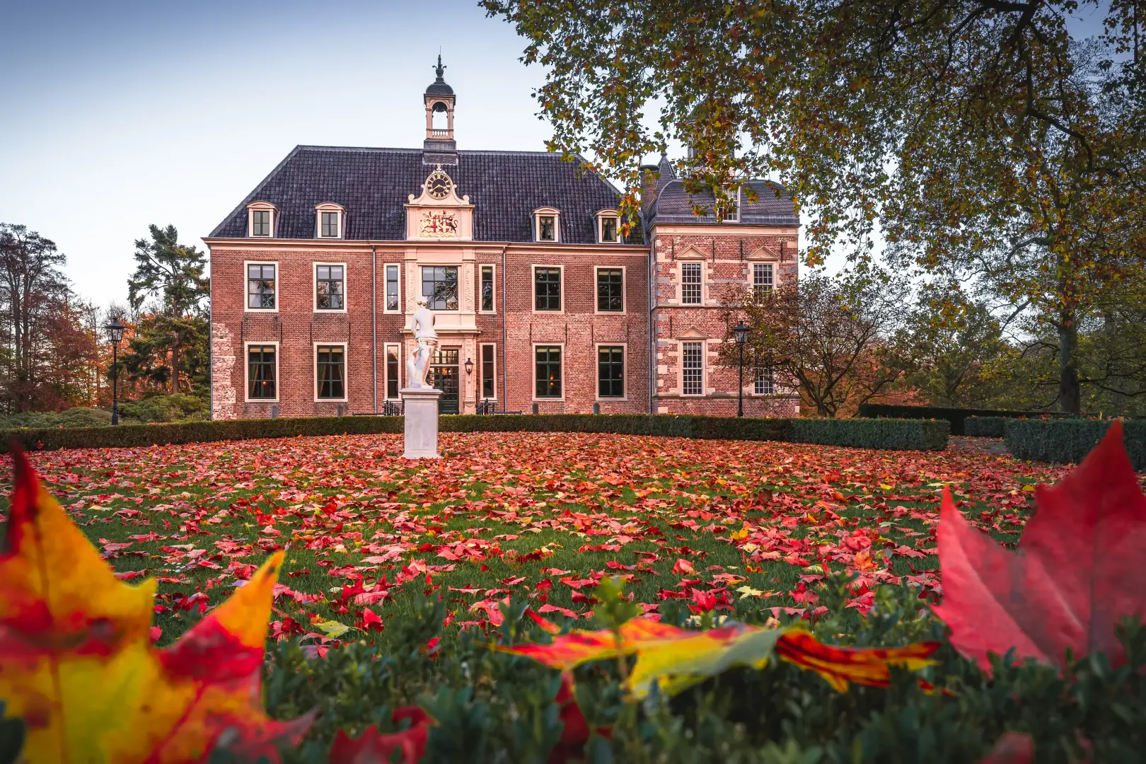 Historisch gebouw met grasveld ervoor waar herfstbladeren op liggen