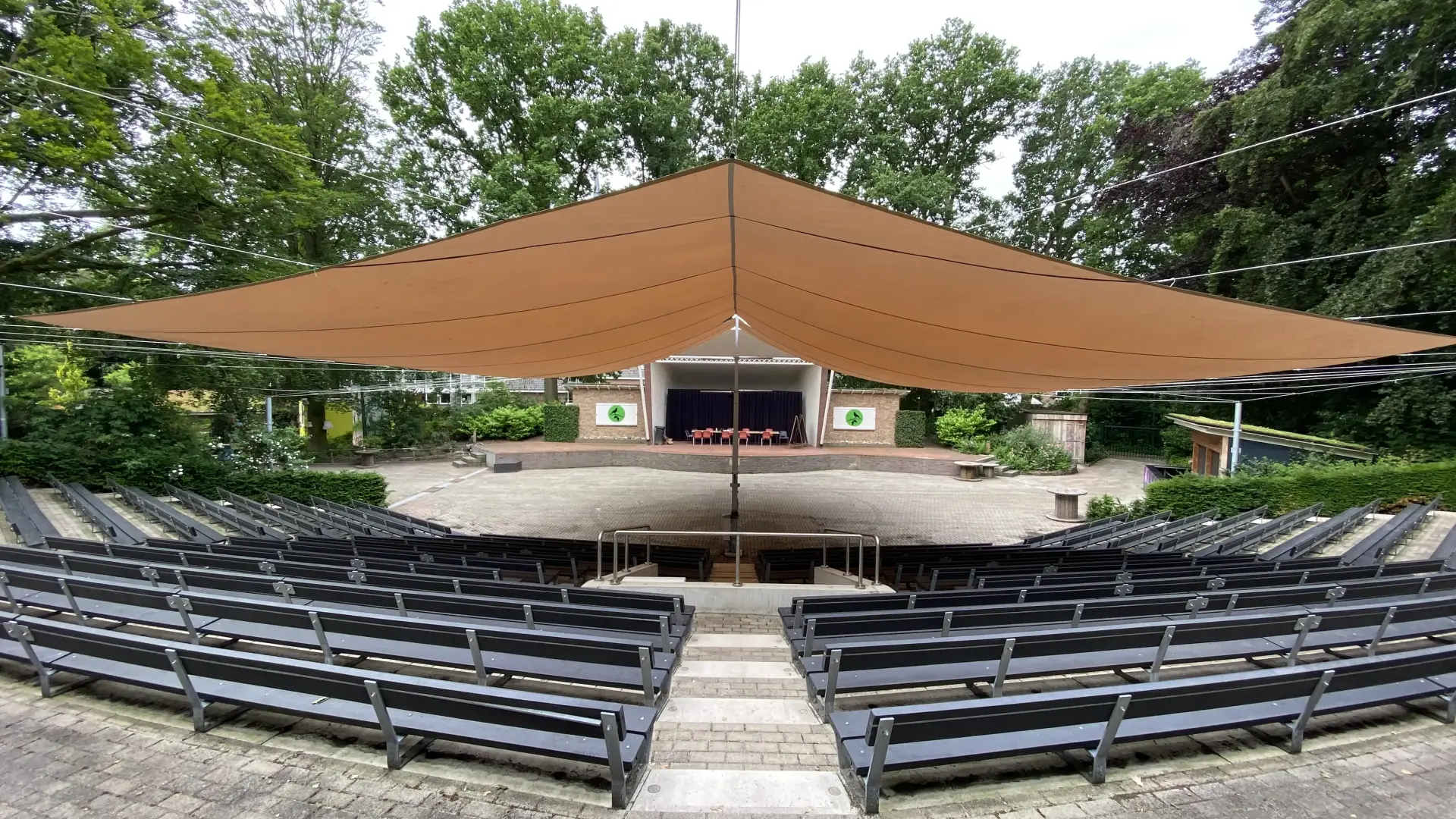 Foto van openluchttheater met bankjes en een podium omringd door bomen